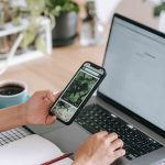 Crop faceless person browsing laptop and smartphone in light room