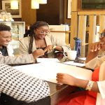 women sitting around a table with pens and papers. They are all laughing