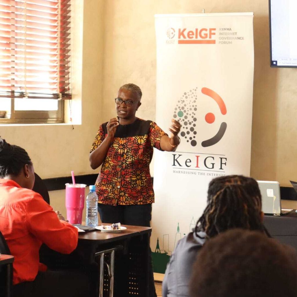 Dr Wambui standing in front of a room of audience. She's speaking with one hand raised