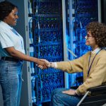 African IT engineer shaking hands with server worker in wheelchair during their work in data center