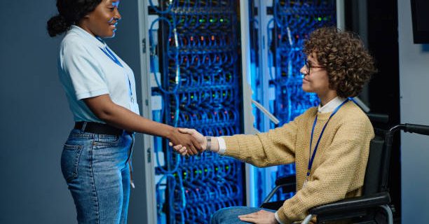 African IT engineer shaking hands with server worker in wheelchair during their work in data center