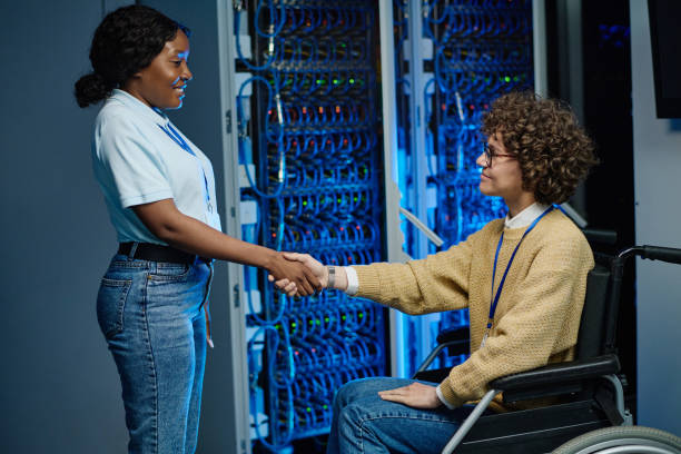 African IT engineer shaking hands with server worker in wheelchair during their work in data center