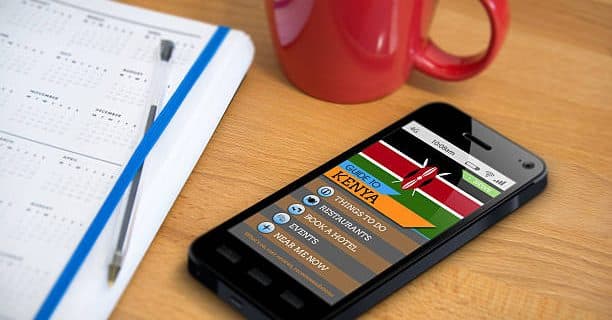 A smartphone showing a travel guide app/website for the country of Kenya - a scene of planning a holiday. Also on the table is a diary/planner and mug.