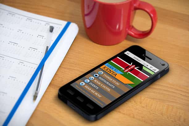 A smartphone showing a travel guide app/website for the country of Kenya - a scene of planning a holiday. Also on the table is a diary/planner and mug.