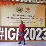 Nic Nyakundi standing in front of the #IGF2023 logo at the KICC in Kyoto