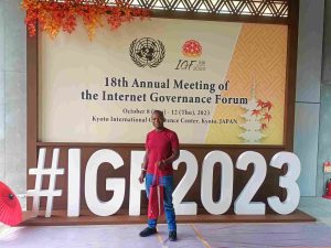 Nic Nyakundi standing in front of the #IGF2023 logo at the KICC in Kyoto
