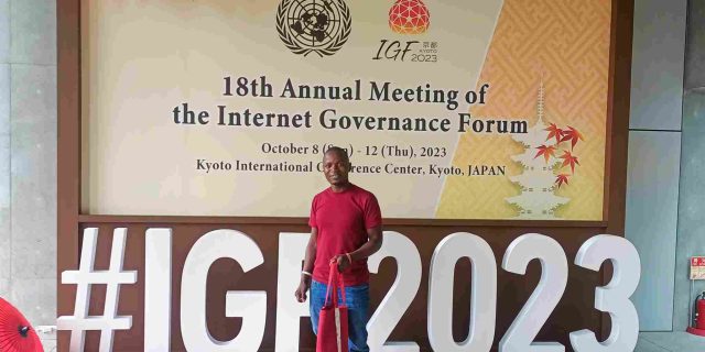 Nic Nyakundi standing in front of the #IGF2023 logo at the KICC in Kyoto