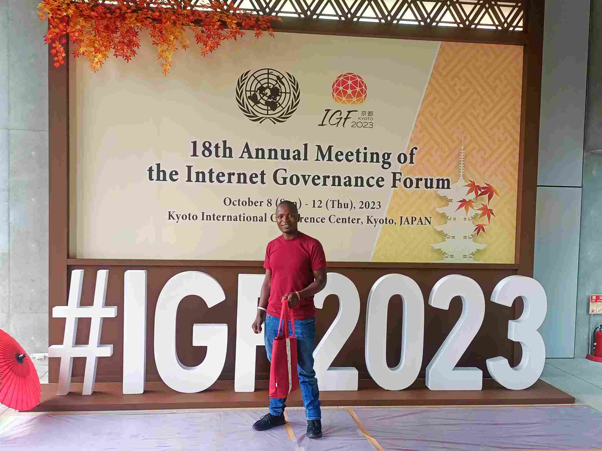 Nic Nyakundi standing in front of the #IGF2023 logo at the KICC in Kyoto