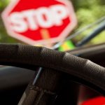 View over the windscreen with a hand holding a steering wheel and a blurred image of the STOP sign in front.